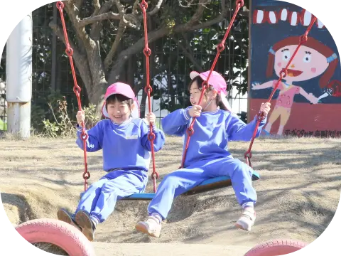 幼稚園のブランコで笑顔を見せる2人の女の子